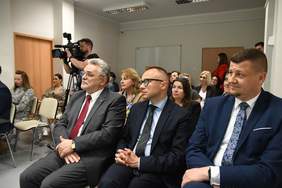 Pokaż zdjęcie: Zdjęcie uczestników otwarcia ośrodka wsparcia i testów, ustawienie krzeseł kinowe, na pierwszym planie mężczyźni w garniturach