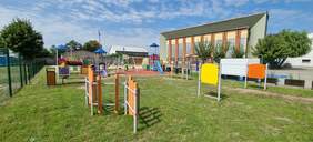 Pokaż zdjęcie: Piękny, nowo wybudowany plac zabaw znajduje się na działce przylegającej do budynku szkolnego. Znajdują się na nim kolorowe huśtawki, drabinki, zjeżdżalnia i inne urządzenia. 