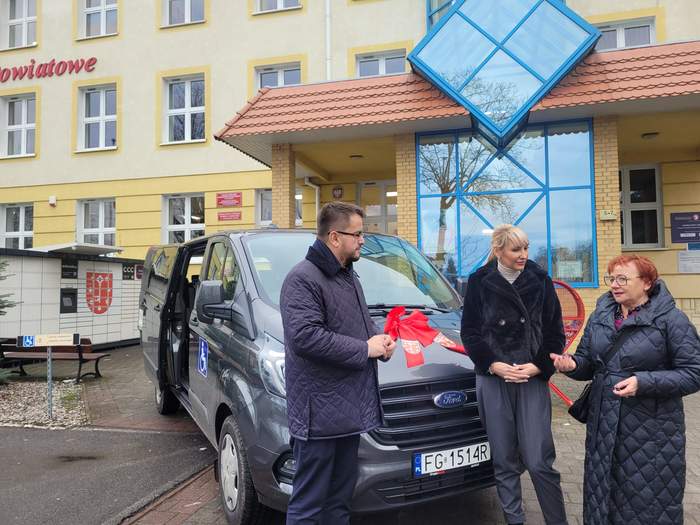 Pokaż zdjęcie: Osoby przekazujące busa stoją i rozmawiają przed budynkiem Starostwa Gorzowskiego