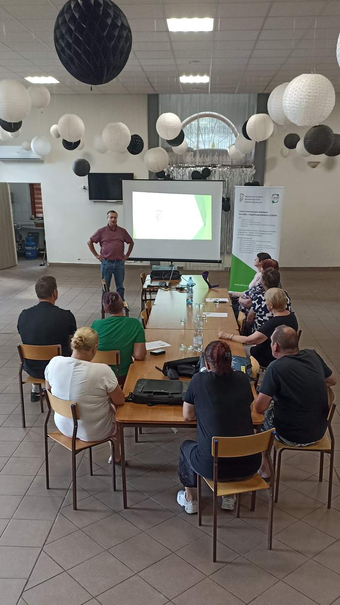 Pokaż zdjęcie: Ujęcie z lotu ptaka gości na sali oraz pracownika PFRON w trakcie prezentacji