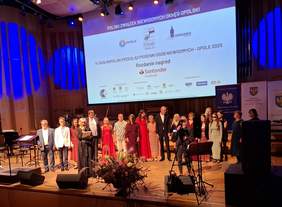 Pokaż zdjęcie: Artyści stoją na scenie koncertowej, otoczeni światłami