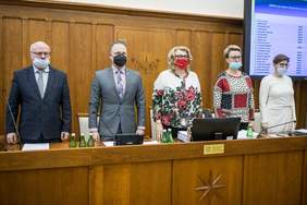 Pokaż zdjęcie: Podczas XXXVIII sesji Sejmiku Województwa Kujawsko-Pomorskiego, przy ławie stoi, przodem do sali, dwóch mężczyzn i dwie kobiety, ubrani  elegancko, w maseczkach