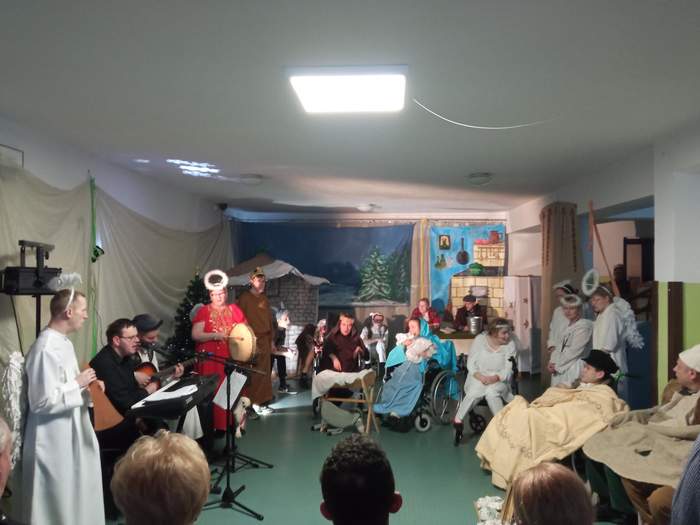 Pokaż zdjęcie: Zdjęcie sceny na której przeprani w aniołki, zwierzęta, trzech króli, kolędników mieszkańcy i pracownicy DPS  śpiewają kolędy.