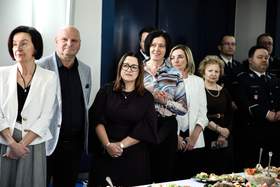 Zdjęcie grupy osób stojących przy stole, mają wzrok skierowany w tym samym kierunku.