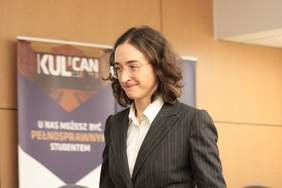 Pokaż zdjęcie: Zdjęcie kobiety w okularach z kręconymi włosami ubranej w garnitur, duże zbliżenie na górną część ciała