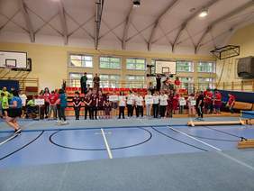 Pokaż zdjęcie: Kilkanaście osób znajduje się na Sali gimnastycznej. Na szyi mają medale.