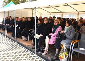 Pokaż zdjęcie: Zdjęcie namiotu pod którym ustawione są krzesełka, siedzą na nich zaproszeni goście. 