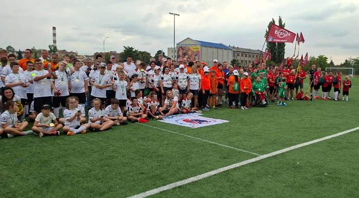 Pokaż zdjęcie: Na trawie boiska stoją wszystkie drużyny pozując do pamiątkowego zdjęcia.