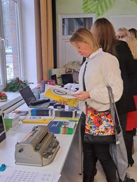 Punkty informacyjne - sprzęt i broszury leżą na stołach, a po prawej kobieta przegląda broszurę informacyjną PFRON