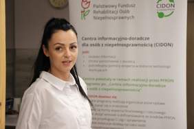 Kobieta na tle roll-upu informacyjnego PFRON i CIDON.
