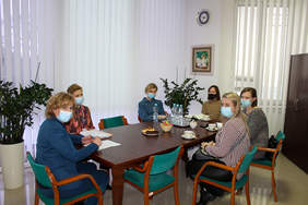 Pokaż zdjęcie: Sześć kobiet siedzących w maseczkach przy brązowym stole, przed nimi leżą dokumenty