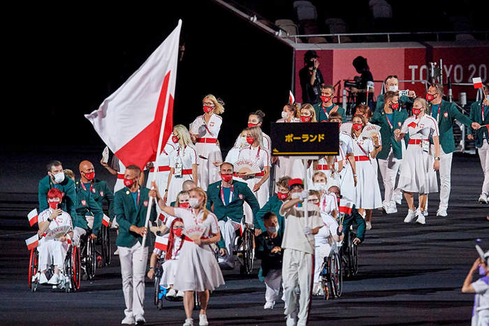 Pokaż zdjęcie: Niepełnosprawni sportowcy w hali z chorążym polskiej reprezentacji z flagą Polski podczas ceremonii rozpoczęcia Igrzysk