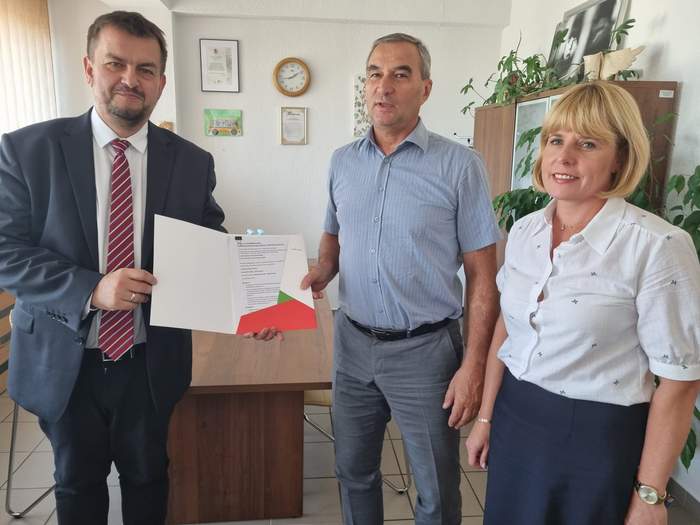 Pokaż zdjęcie: 2 mężczyzn i 1 kobieta stoją obok siebie, w pomieszczeniu biurowym, są ubrani galowo i uśmiechnięci