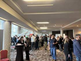 Ludzie rozmawiają z przedstawicielami firm przy stoiskach podczas targów pracy w dużej sali