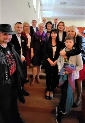 Pokaż zdjęcie: Kobiety i mężczyźni stoją na schodach w Auli. W rękach trzymają róże, dyplomy i statuetki. Wszyscy są uśmiechnięci. Wśród Laureatów na środku stoi dyrektor Marta Mordarska