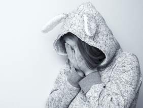 Pokaż zdjęcie: Dziecko ukrywa twarz w dłoniach. Na głowę ma naciągnięty kaptur. Zdjęcie jest szare, brakuje w nim kolorów.  
