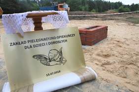 Tablica "Zakład Pielęgnacyjno-Opiekuńczy dla Dzieci i Młodzieży", w tle plac budowy