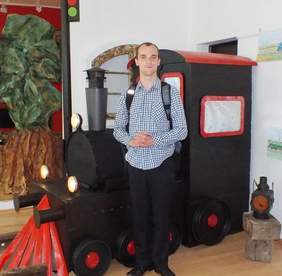 Autor prac - Bartek Pastuszek - na tle lokomotywy - elementu aranżacji wystawy