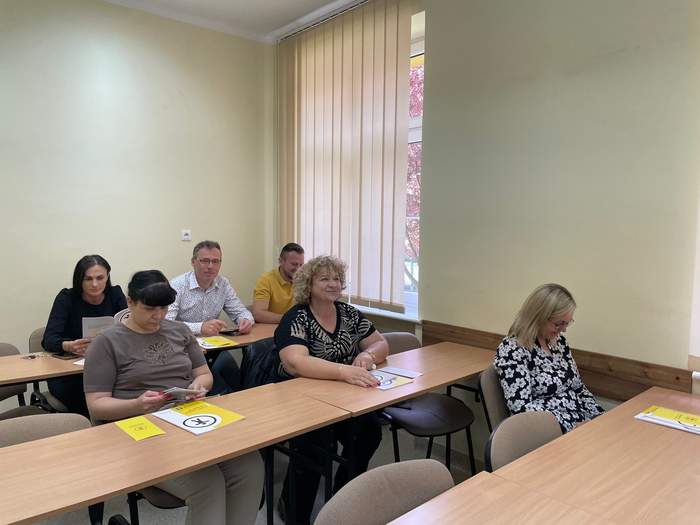 Pokaż zdjęcie: Uczestnicy spotkania siedzą przy ławkach i uczestniczą w dyskusji