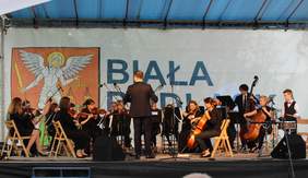 Pokaż zdjęcie: Koncert Orkiestry Społecznej na scenie przed budynkiem ośrodka
