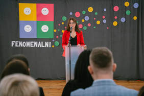 Pokaż zdjęcie: Kobieta stojąca na scenie przemawiająca do gości