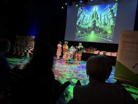 Pokaż zdjęcie: W trakcie spektaklu gra aktorska uczestników i grafika wyświetlna w tle