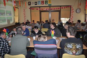 Pokaż zdjęcie: Sala wypełniona dorosłymi uczestnikami siedzącymi przy stołach, zwróconymi w stronę prowadzącego. 