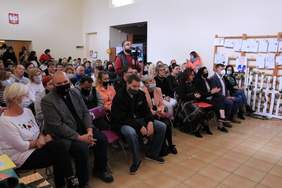 Pokaż zdjęcie: na zdjęciu sala gimnastyczna na której znajduje się grupa osób siedząca na krzesłach ogląda występy artystyczne uczestników WTZ 