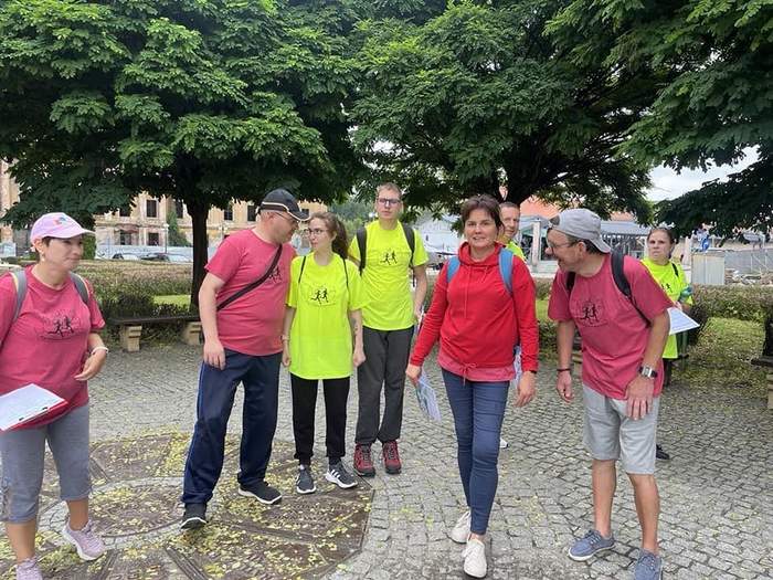 Pokaż zdjęcie: Grupa osób z niepełnosprawnościami stoi na dworze, są ubrani na sportowo, biorą udział w Biegu