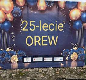 Jubileuszowa dekoracja z napisem „25-lecie OREW”, utrzymana w granatowo-złotej kolorystyce, ozdobiona wizerunkami balonów i kwiatów oraz logotypami instytucji i patronów wydarzenia.
