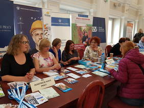 przedstawiciele róznych instytucji siedzą w szeregu przy stole na którym leżą broszury, informatory