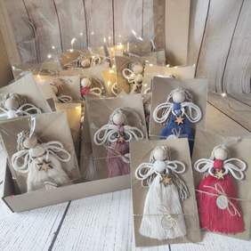 Pokaż zdjęcie: Anioły wykonane są z różnokolorowych sznurków, mają drewniane, okrągłe głowy i są opakowane w przeźroczystą folię. Ułożone są w kilku rzędach. 