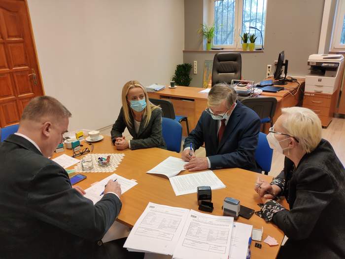 Pokaż zdjęcie: W pomieszczeniu biurowym, przy dużym stole znajdują się 2 osoby reprezentujące Gminę sosnowiec oraz dwóch pracowników PFRON zawierające umowę w ramach OWiT 