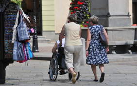Pokaż zdjęcie: Dwie osoby prowadzące wózek inwalidzki na rynku.