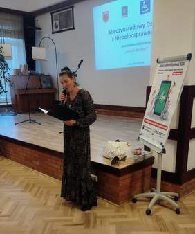 Organizatorka konferencji stoi na środku , przy scenie i czyta