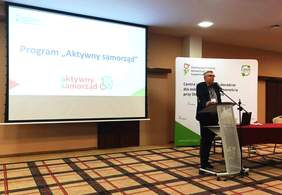 Ekspert ds. współpracy z administracją publiczną w Kujawsko-Pomorskim Oddziale PFRON - Piotr Kopyciński - podczas prelekcji - w tle widoczny jest ekran oraz baner PFRON