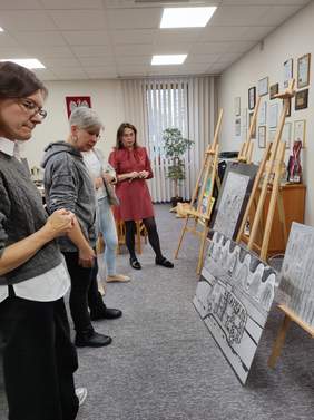 Pokaż zdjęcie: Trzy kobiety stoją przed sztalugami z wystawionymi pracami plastycznymi podczas oceny konkursu w siedzibie PFRON.