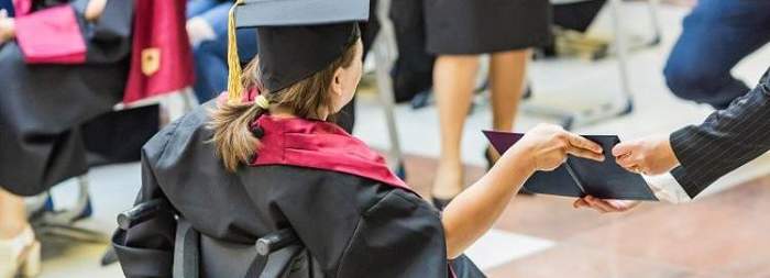 Pokaż zdjęcie: Kobieta na wózku, ubrana w strój żaka odbiera dyplom.