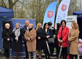 Pokaż zdjęcie: Grupa zaproszonych osób kobiet i mężczyzn, stoi w rzędzie na dworze i czeka na część oficjalną obchodów światowego dnia autyzmu.