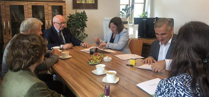 Pokaż zdjęcie: Przy drewnianym stole konferencyjnym siedzi kilka osób, podpisują dokumenty, uśmiechają się do siebie.