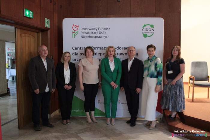 Pokaż zdjęcie: Na scenie pod banerem CIDON stoi grupa 7 osób pozując do pamiątkowego zdjęcia.