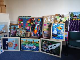 Pokaż zdjęcie: W pokoju z niebieską wykładziną wyeksponowane są prace plastyczne z kategorii płaskorzeźba.