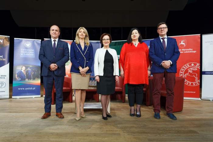 Pokaż zdjęcie: na scenie stoi pięć osób, które przed chwilą podpisały umowę porozumienia pomiędzy pięcioma uczelniami. Od lewej mężczyzna w garniturze, następnie trzy kobiety oraz mężczyzna w garniturze