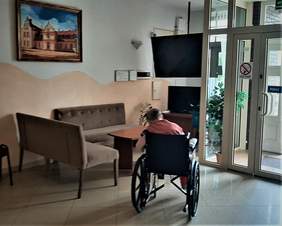 W kąciku telewizyjnym ośrodka, na wózku inwalidzkim siedzi kobieta, tyłem do obiektywu