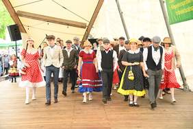 Pokaż zdjęcie: Na scenie występuje grupa dzieci przebranych w kolorowe stroje.