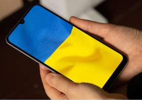 Pokaż zdjęcie: Zbliżenie na dłonie, które trzymają telefon z ukraińską flagą na ekranie
