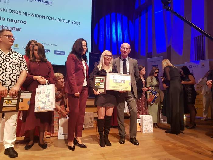 Pokaż zdjęcie: Grupa ludzi na scenie trzymająca nagrody. W centrum stoi zwyciężczyni - Pani Anna Wereszczyńska - w towarzystwie Pana Tomasza Dłubaka - Dyrektora Oddziału Opolskiego PFRON
