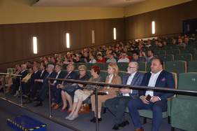 Pokaż zdjęcie: Na dużej sali kinowej w stopniowo podwyższanych rzędach siedzi kilkadziesiąt osób