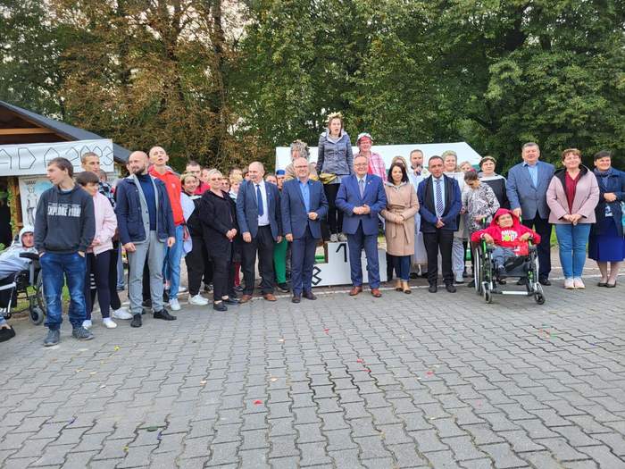 Pokaż zdjęcie: Zdjęcie na dworze, na tle namiotów, stoi grupa osób i pozuje do zdjęcia.