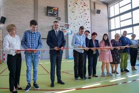 Pokaż zdjęcie: 5 kobiet i 5 mężczyzn stoją w rzędzie w dłoniach trzymają nożyce, którymi przecinają wstęgę. 